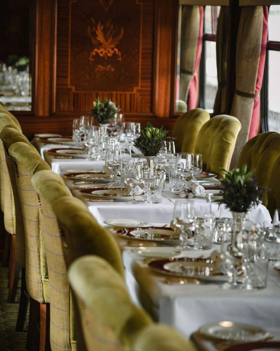 un salon de luat masa dintr-un vagon de trenuri internaționale de lux, cu scaune verzi și veselă scumpă