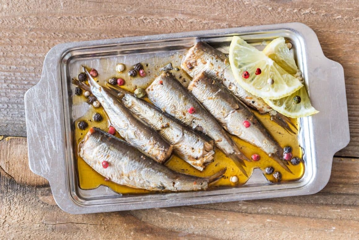 pe o tava de inox dreptunghiulara cu manere sunt asezate 6 sardine fără cap, preparate cu lamaie, ulei de masline și boabe de piper mozaic. Diferena între anșoa și sardine