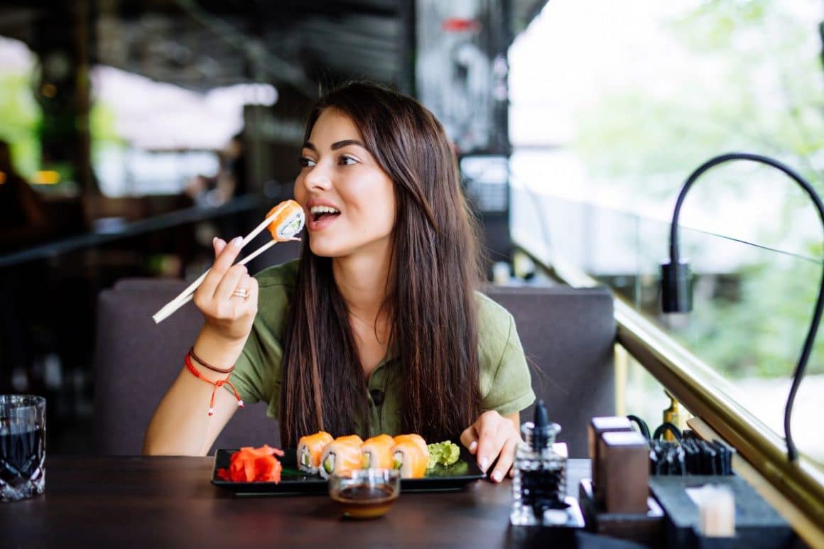 o fata tanara sta la masa unui restaurant li mananca sushi cu betisoarele chinezesti. Cum se mănâncă sushi