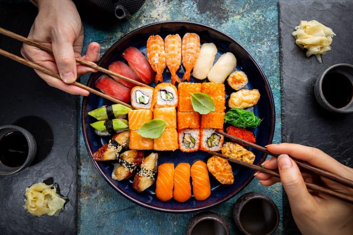 un cuplu de tineri impart un platou rotund de sushi pe care sunt mai multe feluri de sushi. 