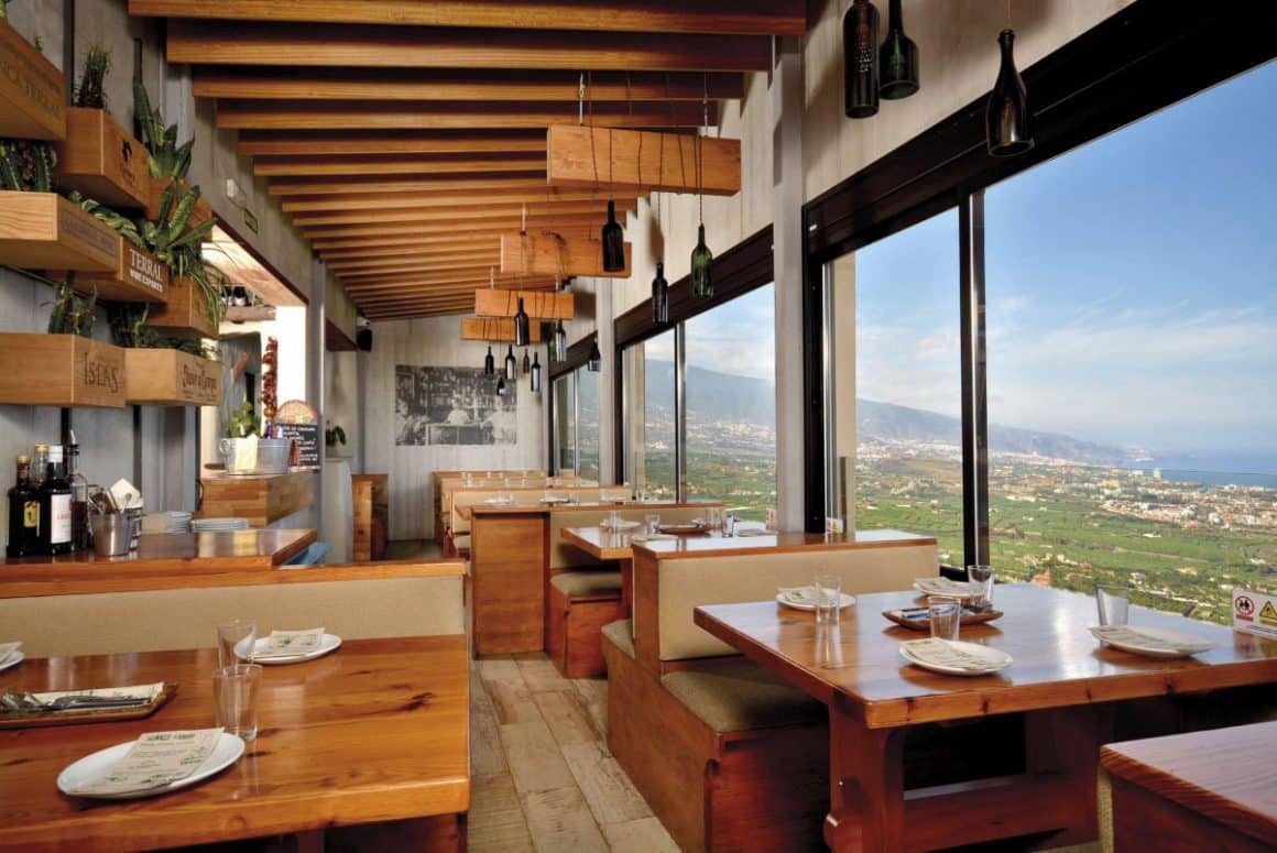 interiorul restaurantului El Calderito de La Abuela, cu mese de lemn și banchete tapitate, in apropierea unui perete de sticla pe care se vede un peisaj natural
