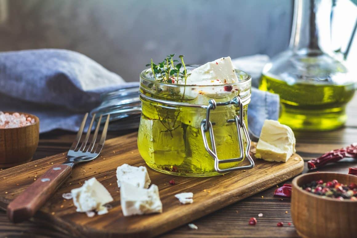 Feta cheese marinated in olive oil with fresh herbs in glass jar. Wooden background. rețete fără foc