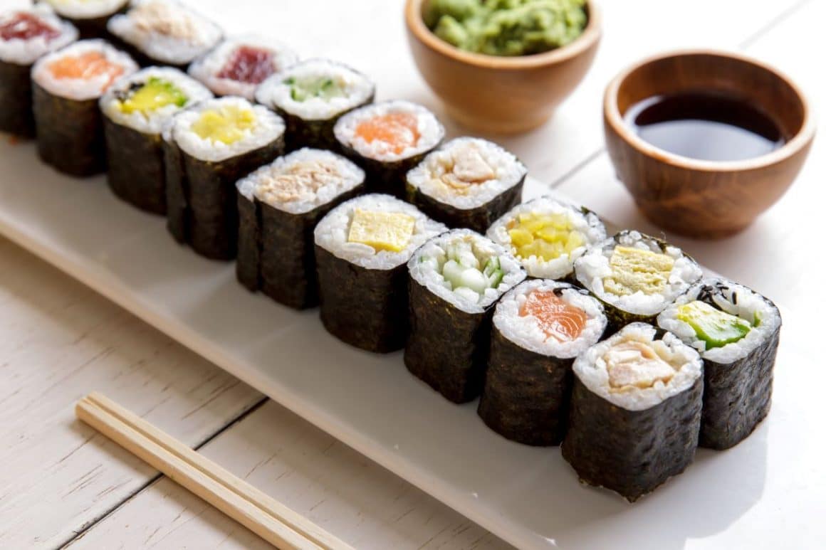 un platou lung, alb, de sushi maki, iar langa el sunt doua boluri mici de sos de soia și de wasabi. Cum se mănâncă sushi