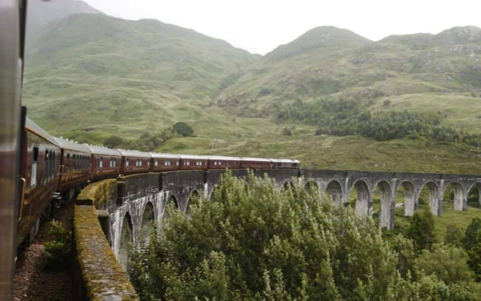 un tren international de lux trece peste un viaduct de piatra, intr-un peisaj montan verde