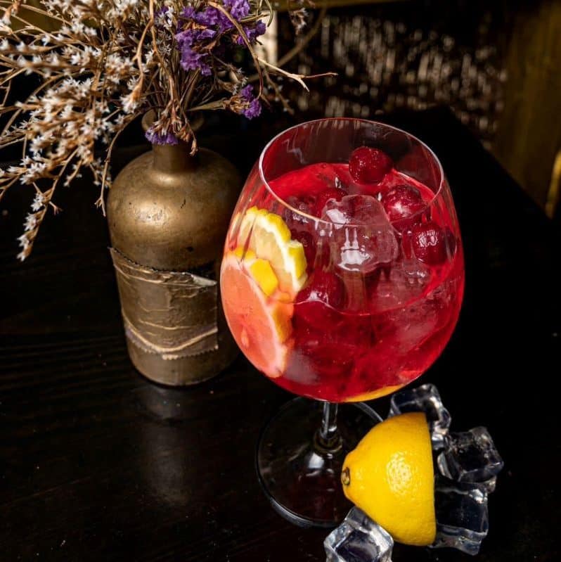 un pahar de cocktail cu picior este asezat pe o masa, alaturi de un vas cu flori uscate
