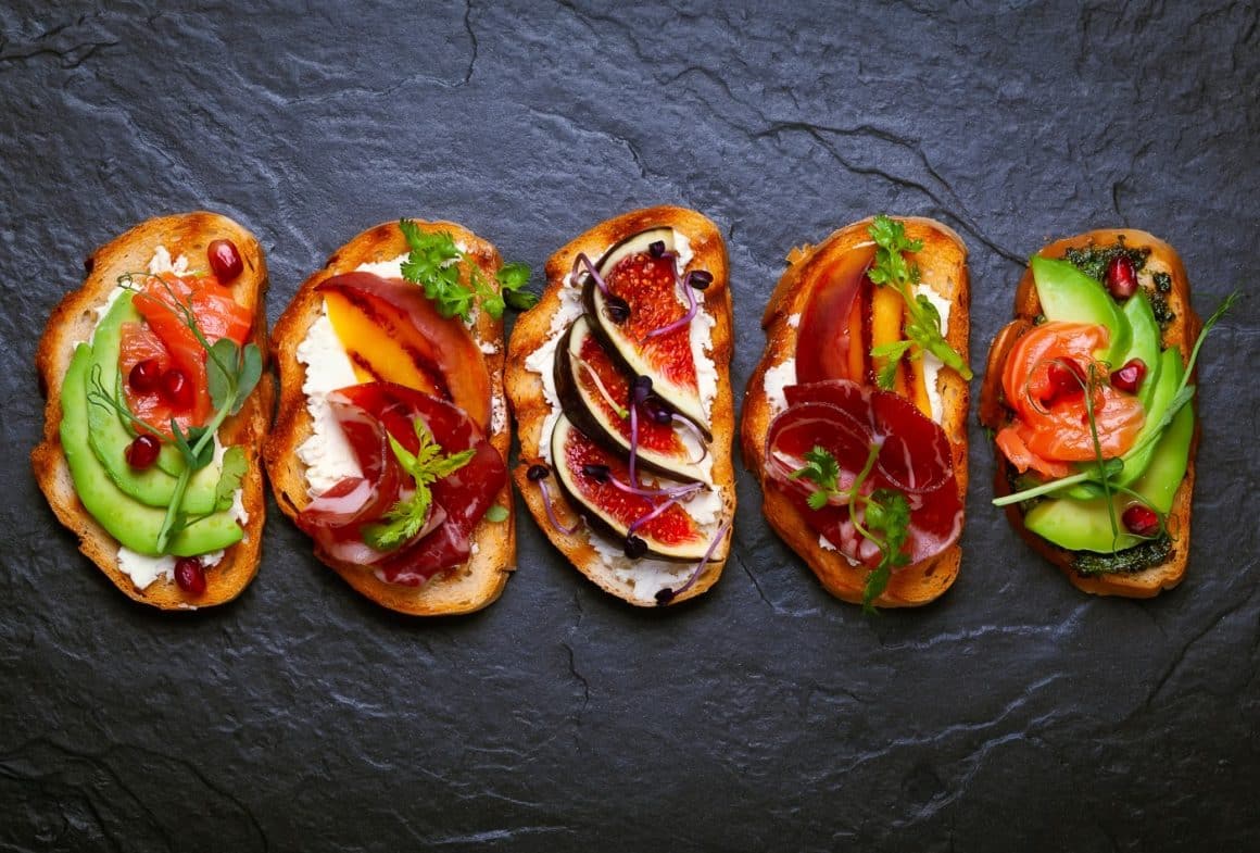 mai multe variante de sandvișuri, cu diferite toppinguri, fotografiate pe fundal negru. Idei pentru mic dejun