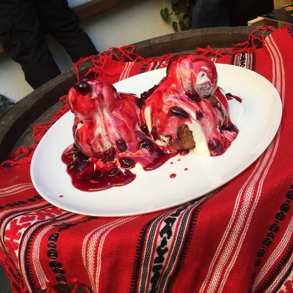 close up cu o farfurie cu 2 papanasi cu smantana si dulceata, asezati pe un stergar rosu cu motive traditionale, de la Bodega La Mahala, unde mâncăm papanași buni în București