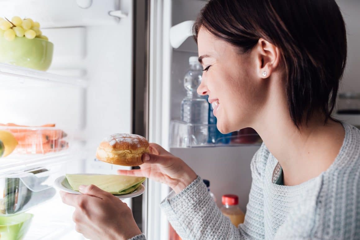 Woman having an unhealthy snack, she is taking a delicious pastry out of the fridge
