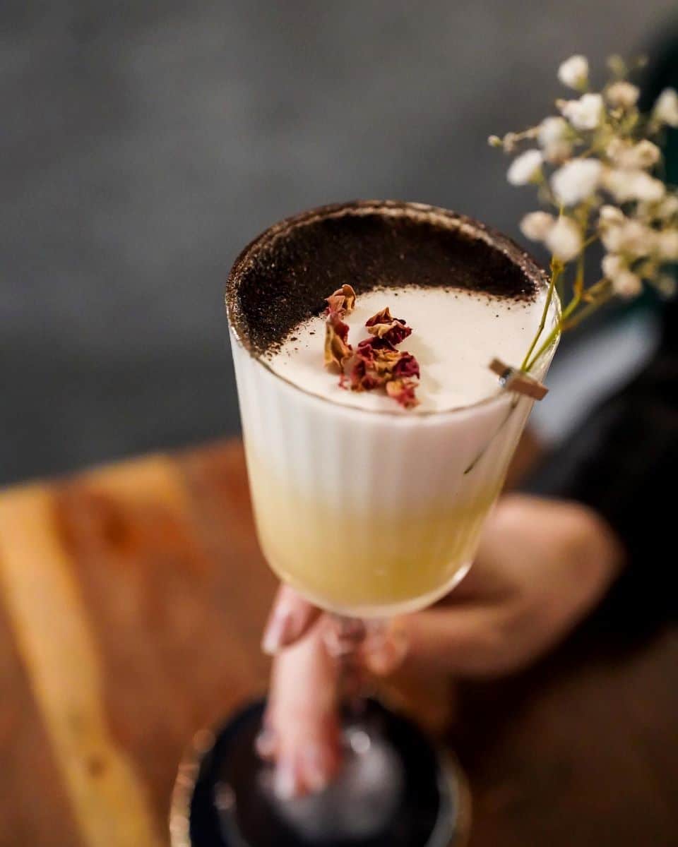 o mana de femeie tine ridicat un pahar de cocktail ornat cu pudra de cacao și câteva flori albe