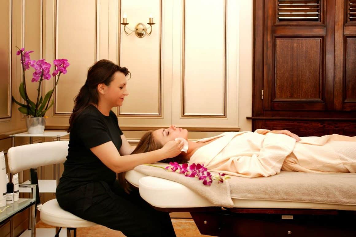 o femeie ii face un masaj facial unei alte felei, ininstă pe o masă de spa în românia