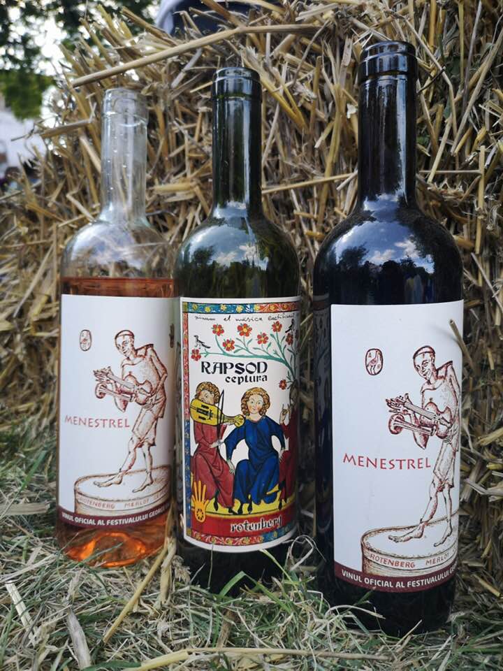 trei sticle de vin asezate pe iarba, in fata unui balot de paie