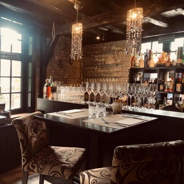 Interiorul restaurantului One din Bruges, cu scaune confortabile, pereti din caramida, bar plin de sticle si pahare si candelabre din cristal