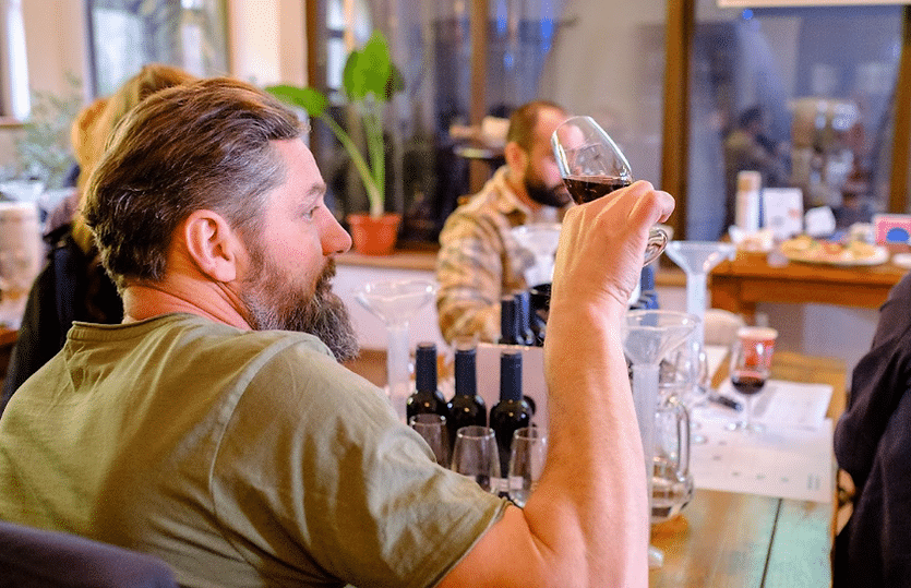un barbat priveste atent la paharul de vin pe care-l degustă, in cadrul unei sesiuni de degustare pe drumul vinului