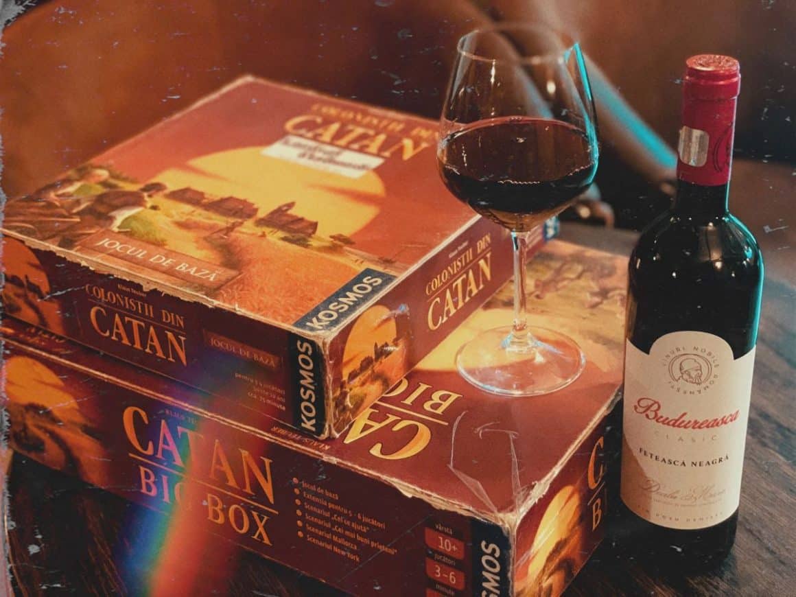 cutia unui board game este așezată alături de o sticlă de vin roșu și un pahar