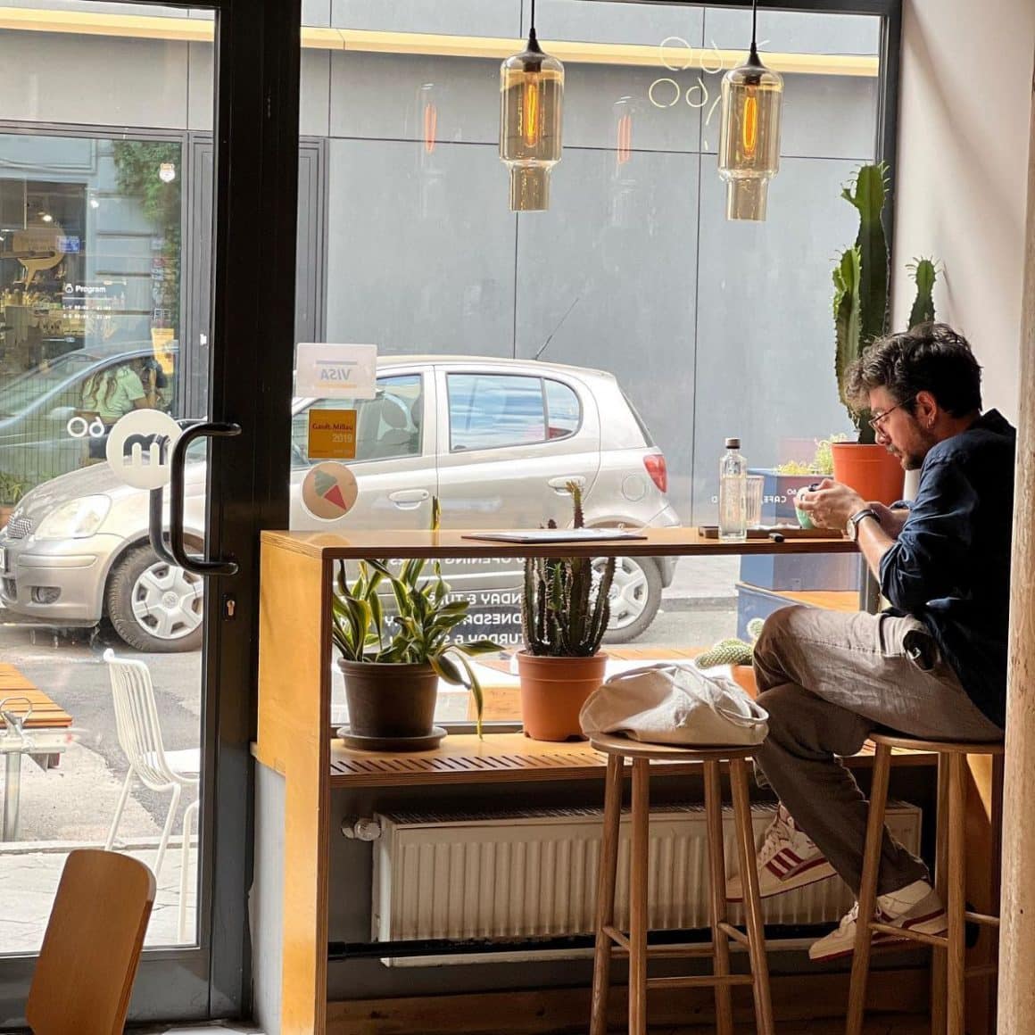 un bărbat tânăr îți bea caufeauaîn fata unui geam mare dintr-o cafenea cu aer scandinav din bucuresti