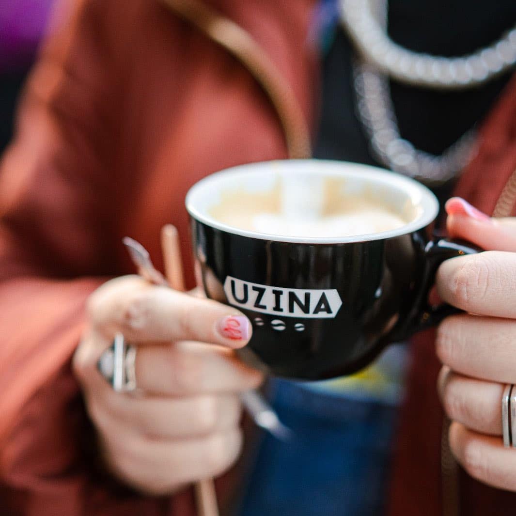 o femeie tânără ține cu ambele mâini o ceașcă de cafea