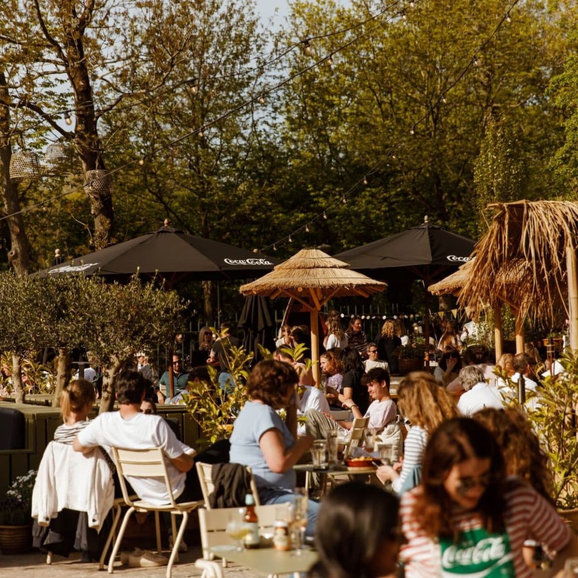 mai multi oameni iau masa sau beau un pahar la una dintre terasele dintr-un parc din amsterdam