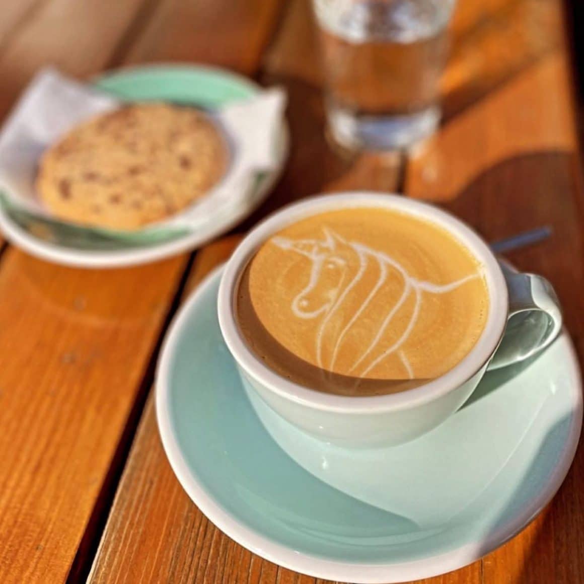 o ceasca albă de cafea cu latte artpe o masă de lemn, și un cookie lângă