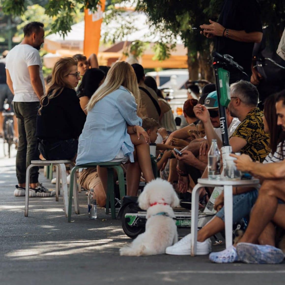 mai multi tineri socializează în fata unei cafenele micute din bucuresti, stând la mese sau pe trotoar