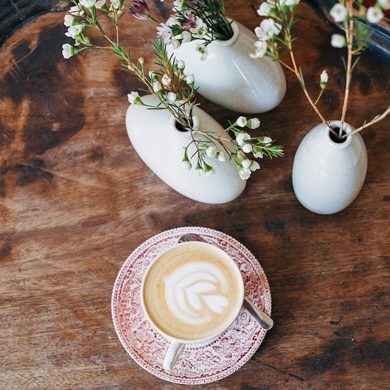 o ceașcă elegantă de porțelan cu cafea este asezată lângă câteva vase decorative cu flori albe in ele
