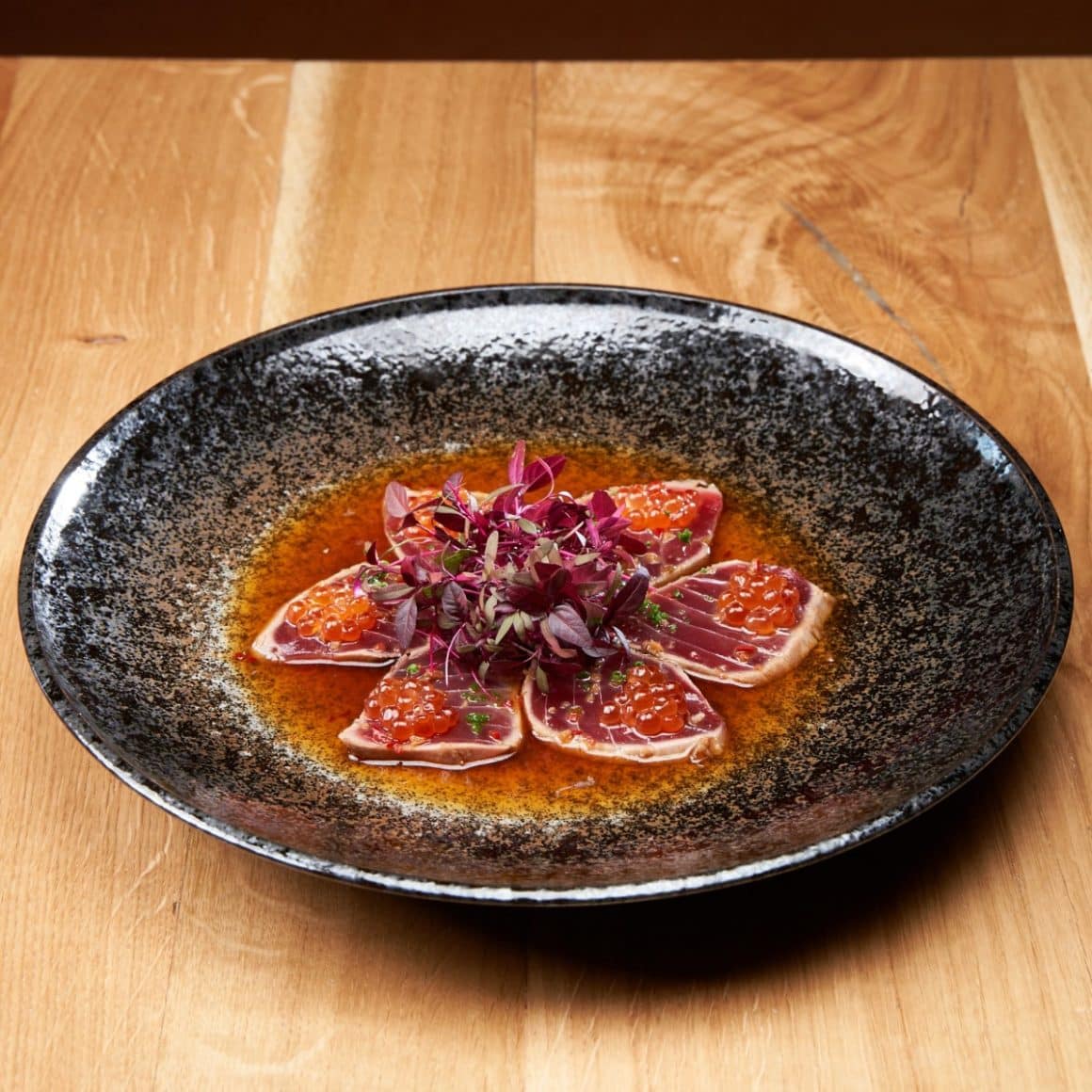 tonul BlueFin tăiat în stil sashimi, asezonat perfect cu sos ponzu, o atingere picantă de ardei iute și completat de textura crocantă a caviarului roșu.