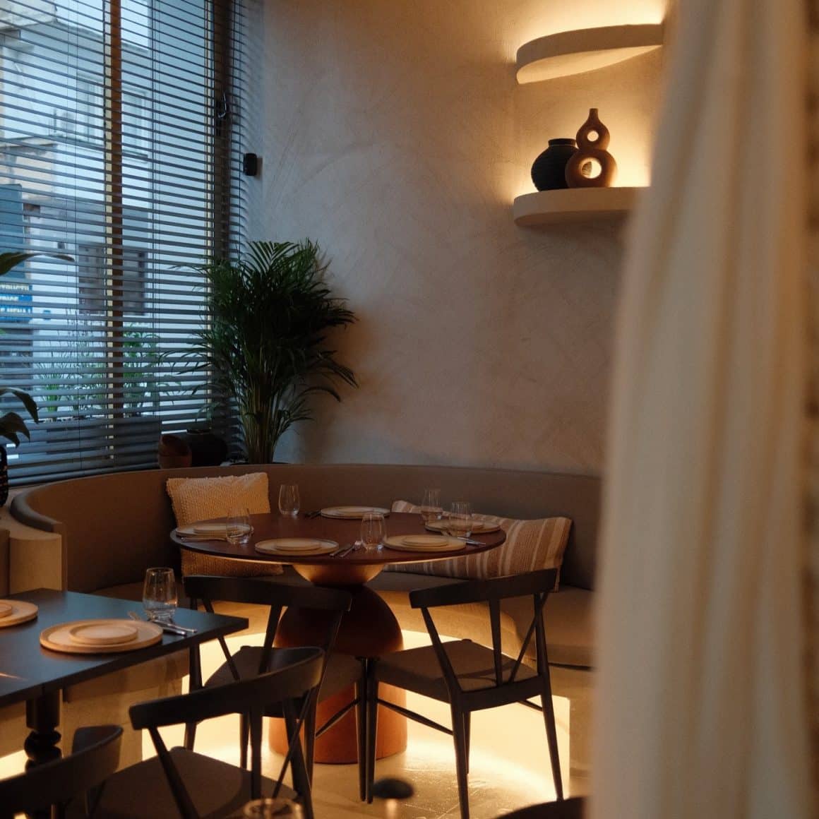 Masa circulara din restaurantul Must, fotografiata pe inserat, cu luminile aprinse in restaurant. O atmosferă caldă. restaurante cozy din București 