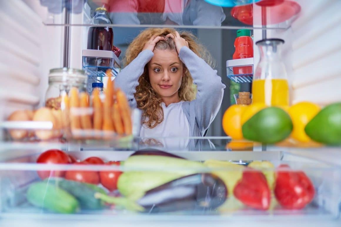o femeie se uita descumpănită în frigider. Cum să-ți organizezi mai bine frigiderul