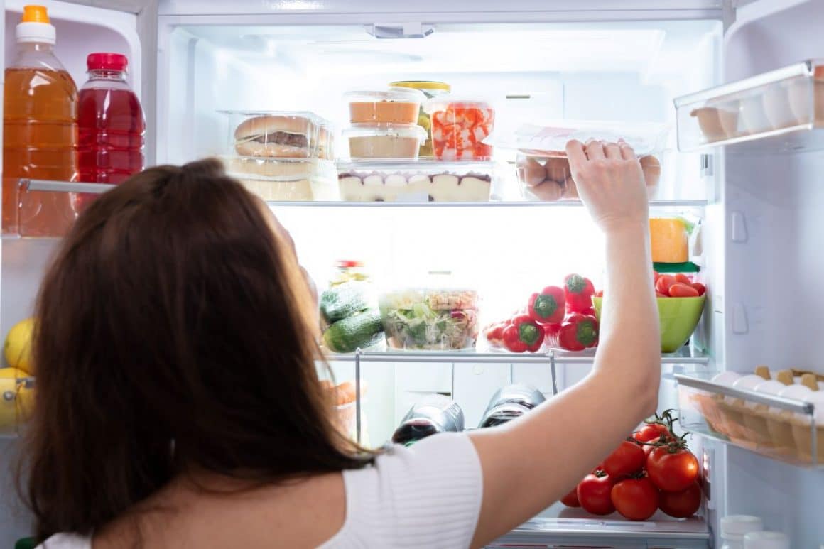 o femeie tânără pune in frigider o caserola transparentă, lângă alte caserole. Cum să-ți organizezi frigiderul