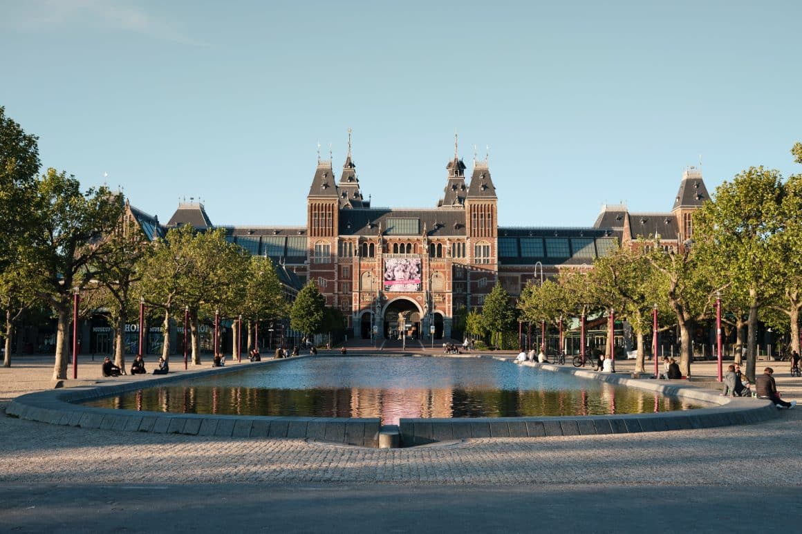Rijksmuseum, unul dintre principalele muzee ale amsterdamului, cu un lac artificial in față și copaci pe ambele părți