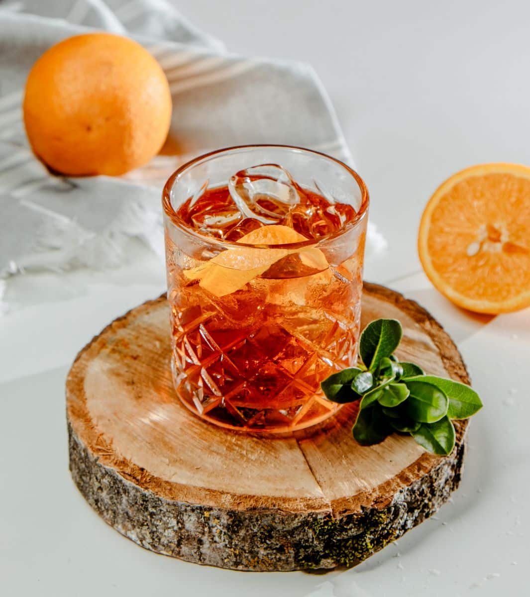 un pahar de Sidecar cu rom și suc mandarine, unul dintre mai multe cocktailuri de toamna, pe o rondea de elmn și două portocale in jurul lui