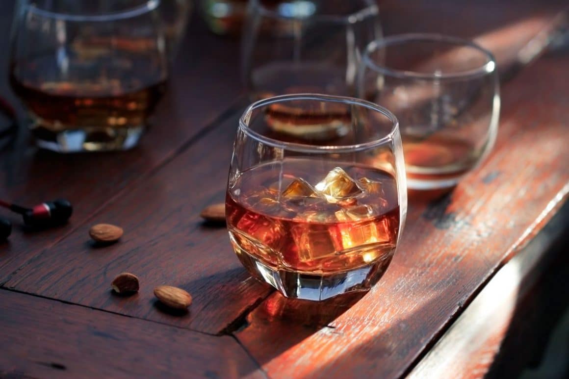 mai multe pahare de whiskey sour sunt asezate pe o masă de lemn, cu câțiva sâmburi de migdale în jurul lor