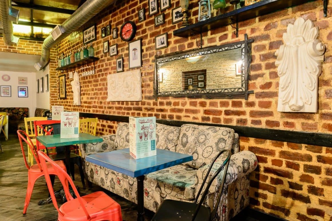 mai multe mese, scaune și o canapea, in interiorul unui bar, cu un perete de cărămidă aparentă și multe decorațiuni