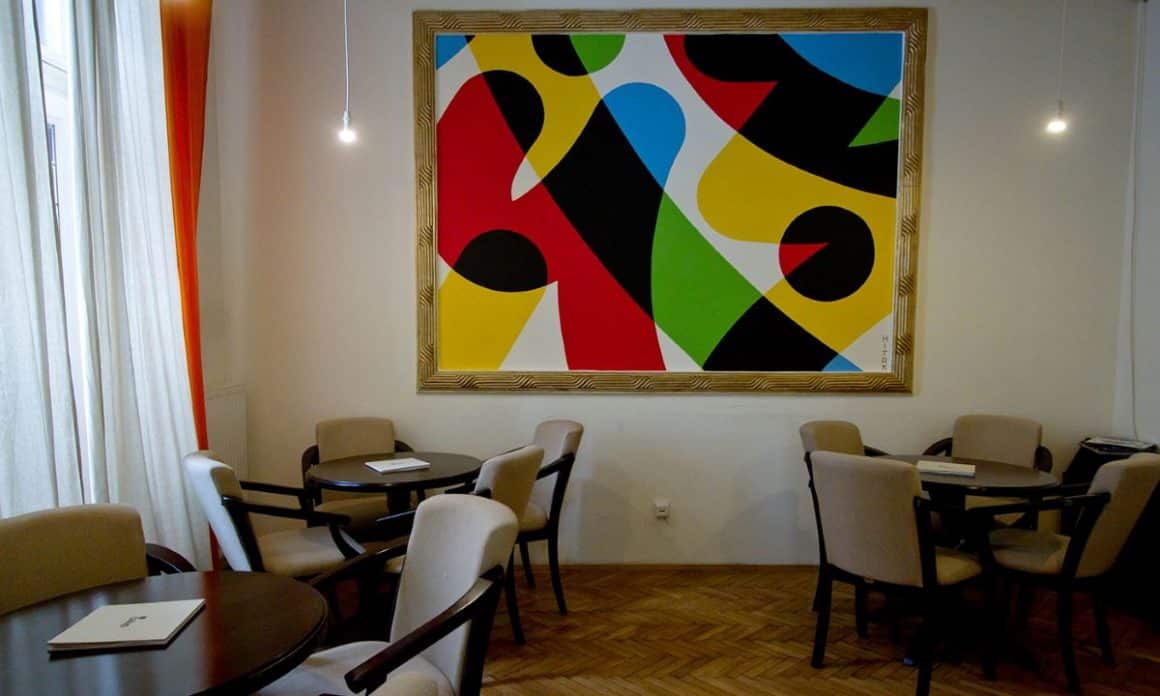 un tablou modern este asezat pe peretele din dreptul mai multor mese și scaune de restaurant