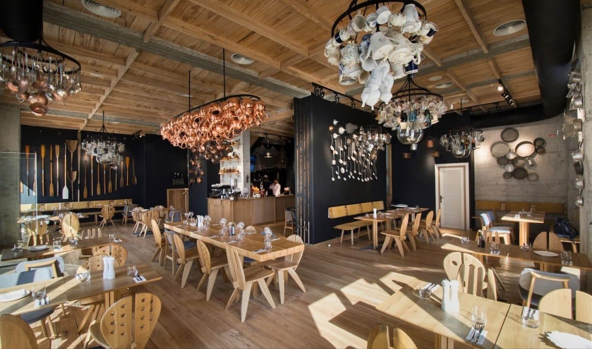 interiorul restaurantului Sardin, cu mese si scaune din lemn, cu spatar in forma de tacamuri, si cu corpuri de iluminat realizate din oale, polinice si pahare, unul din restaurante cozy din București