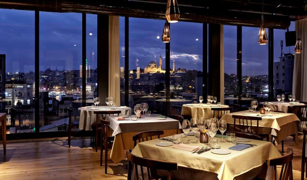 Restaurantul Neolokal din Istantbul, fotografiat seara, cu mese elegante si priveliste spre moschee
