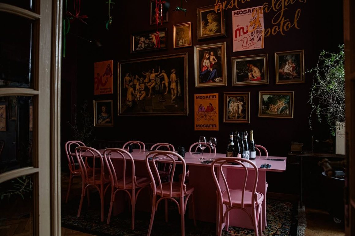 Bistrouri București: Mosafir, bistro din București cu interior eclectic, mese și scaune roz, pereți burgundy decorați cu tablouri și lumină ambientală caldă.