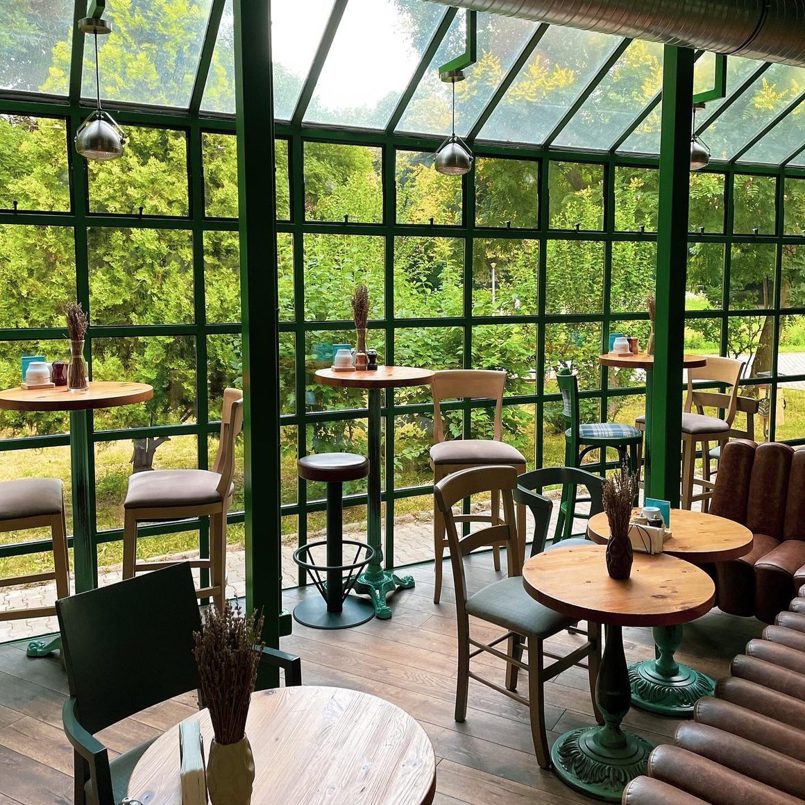 B4 Market, spațiu de dining luminos, cu pereți vitrați, mese din lemn și vedere spre grădina verde.
