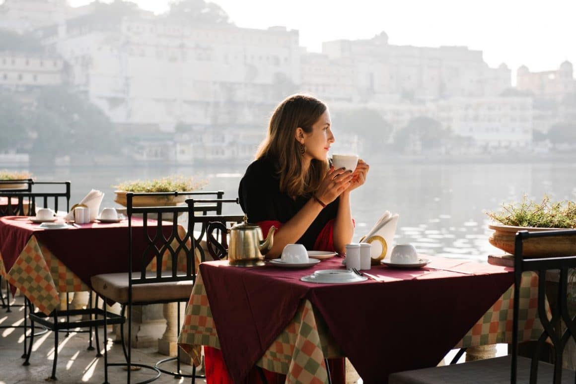 o femeie bea un ceai cât timp așteaptă mâncarea, la un restaurant de lângă malul mării