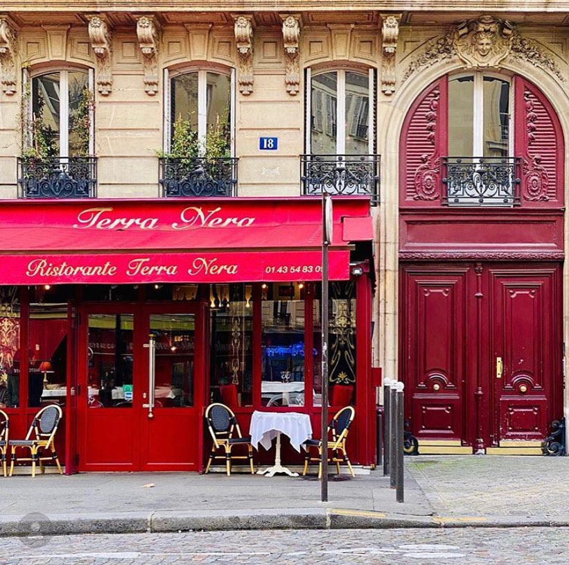 Intrarea in restaurant Terra Nera din Paris, fotografiat de la distanta, cu copertina rosie si exterior vopsit in rosuș. Restaurantul lui gabriel din serialul Emily in Paris