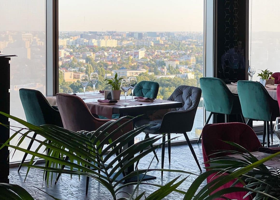 masa eleganta, de 4 persoane, cu scaune din catifea, amplasata in fata unei ferestre mari prin care se vede panorama orasului, la restaurant 18 Lounge. Restaurante la înălțime din București