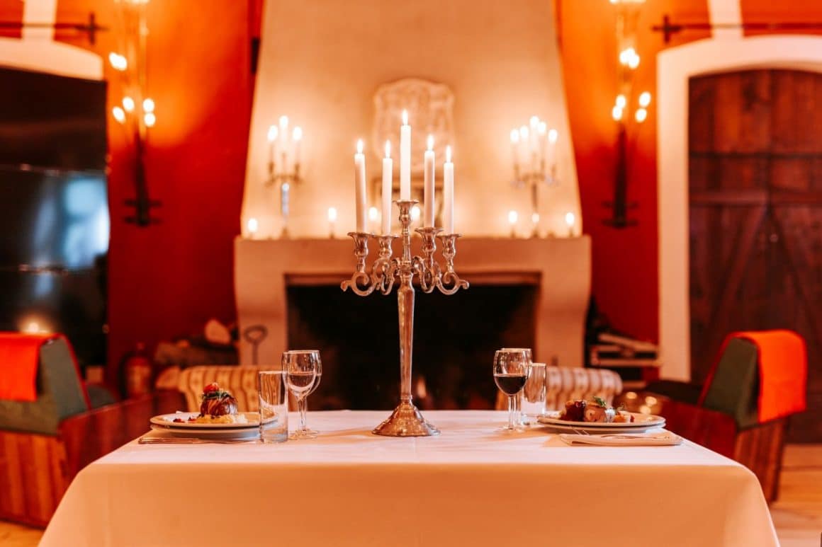 prim plan cu o masa aranjata pentru o cina romantica, decorata cu un candelabru cu lumanari, iar in fundal un semineu