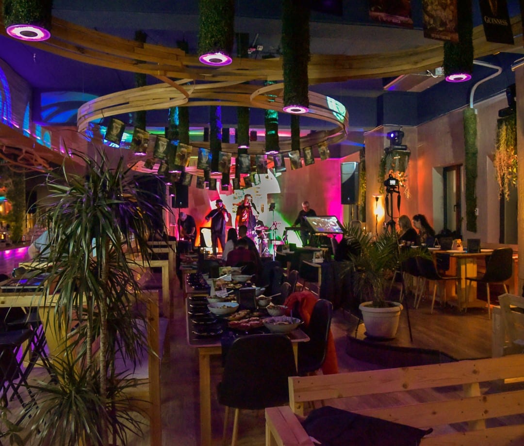 imagine din interiorul restaurantului Balkon restogarden, cu mese de lemn, plante decorative si iluminat teatral, iar in fundal un concert live pe scena.