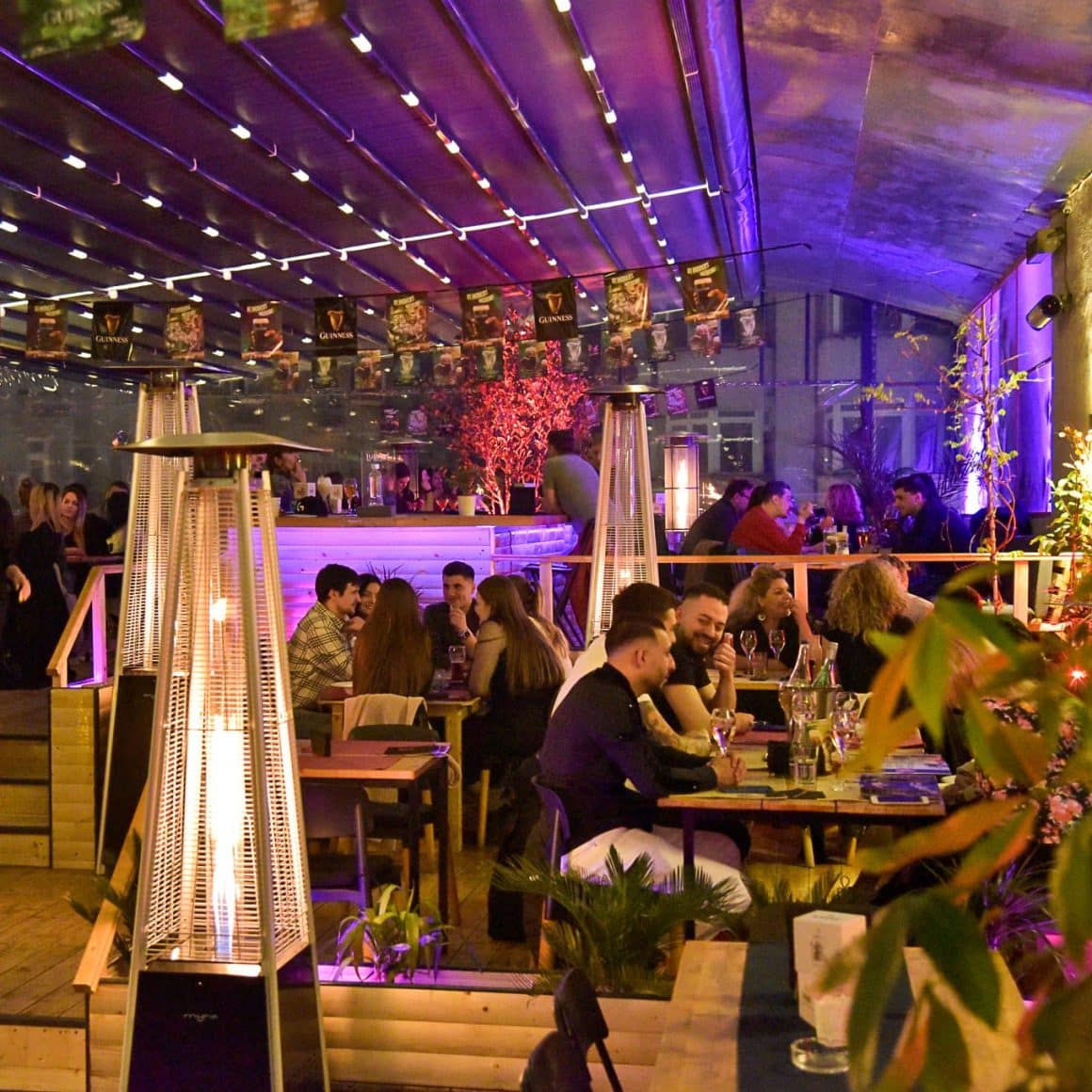 Oameni asezati la mese si la bar pe terasa la Balkon Resto Garden, unul din restaurante la înălțime din București
