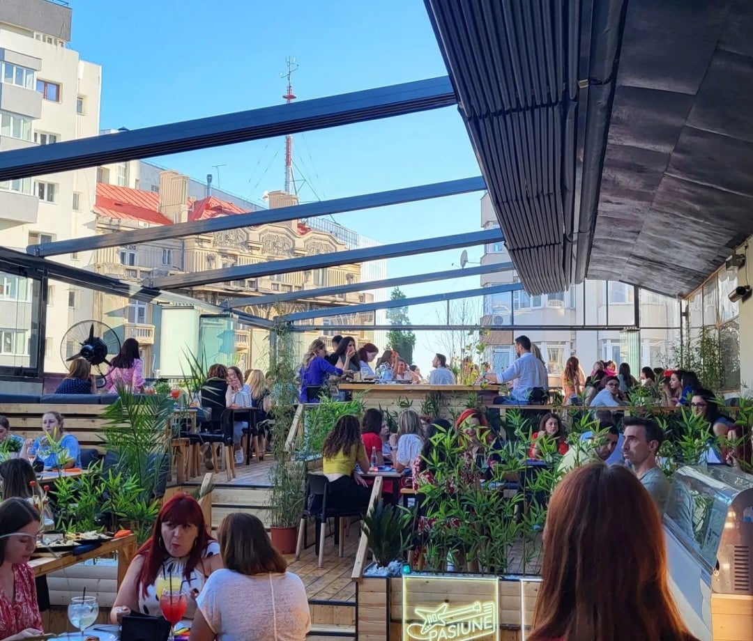 Oameni asezati la mese si la bar pe terasa la Balkon Resto Garden, unul din restaurante la înălțime din București