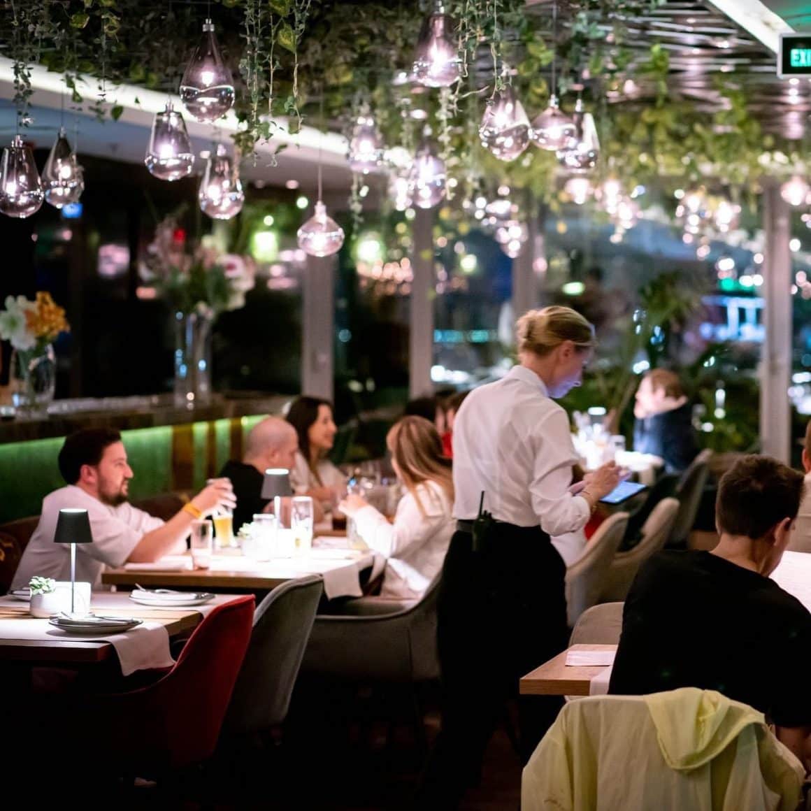 Mai multi oameni iau cina la restaurant 18 Lounge, decorat cu multe luminite decorative atarnate de tavan si plante ornamentale. lRestaurante la înălțime din București