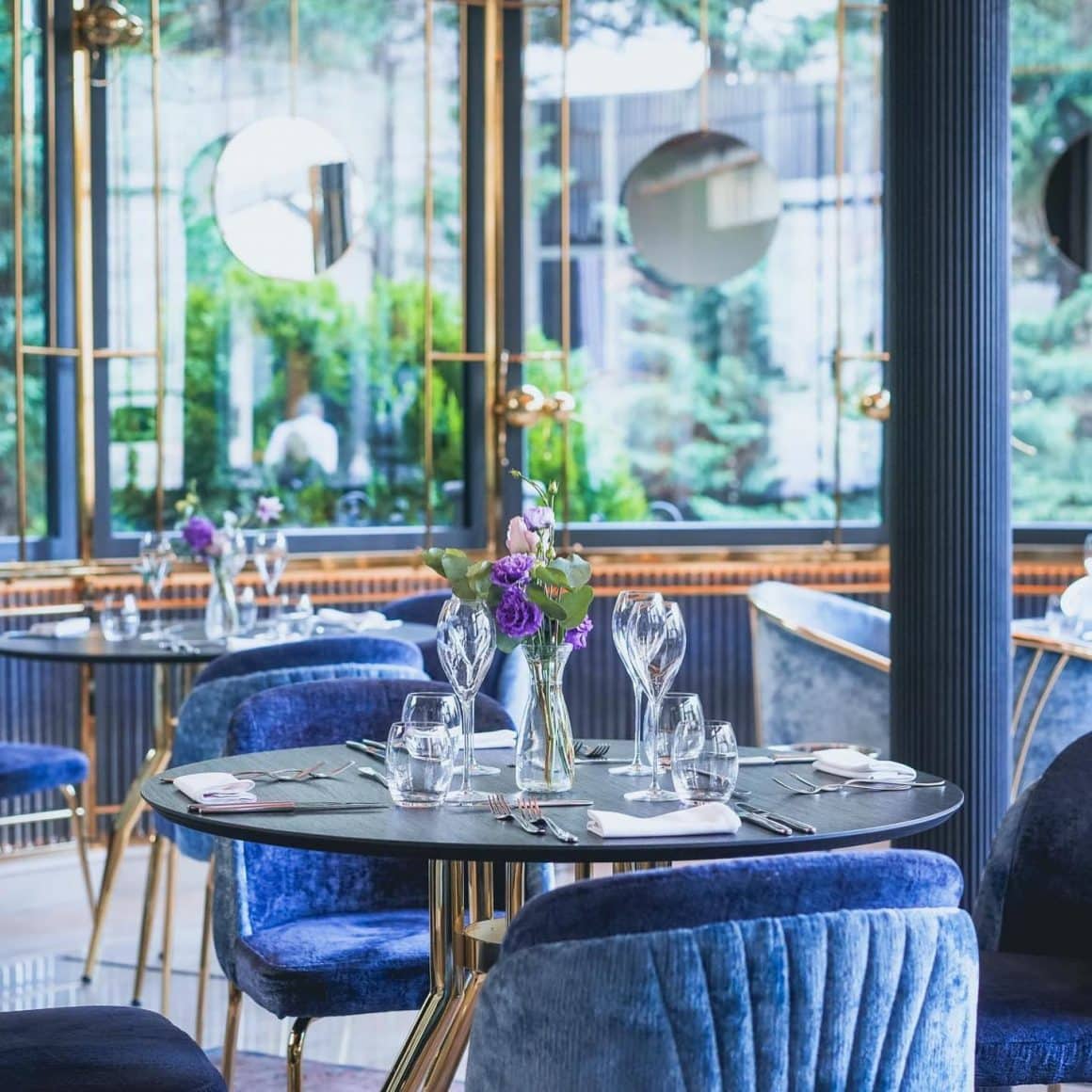 masa eleganta de 2 persoane, cu flori si pahare de vin pe masa si scaune din catifea albastra la restaurant L'Atelier Relais & Chateaux. Cină-experiență București