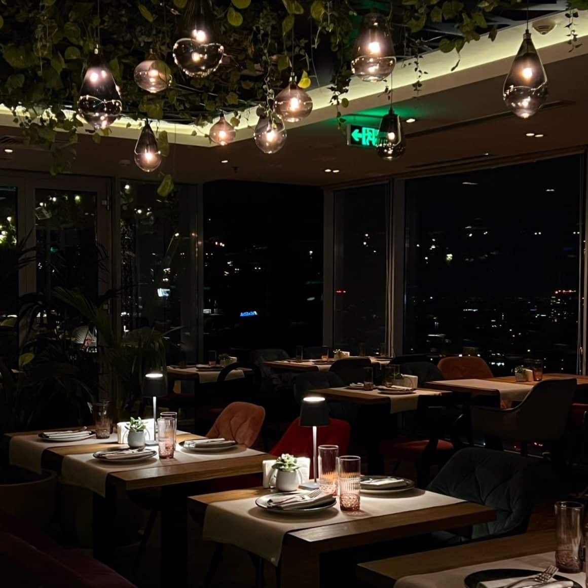 mese iluminate discret in restaurantul 18 Lounge, fotografiat seara, prin ferestrele caruia se vede orasul de sus