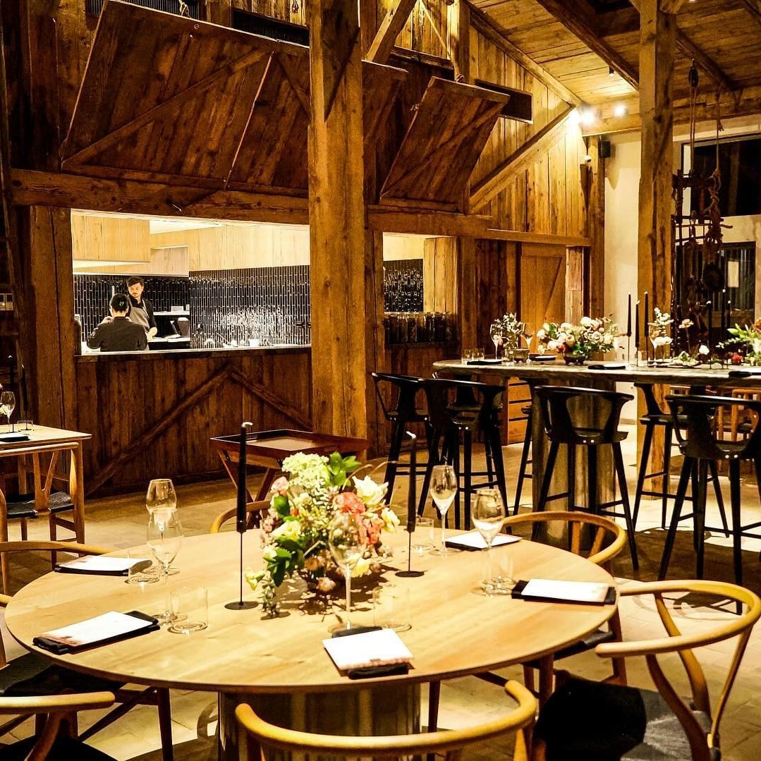 restaurantul La Hambar fotografiat seara, cu sala de mese cu lumini aprinse si mese aranjate elegant, cu pahare de vin si flori. In fundal, bucataria deschisa.Cină-experiență București