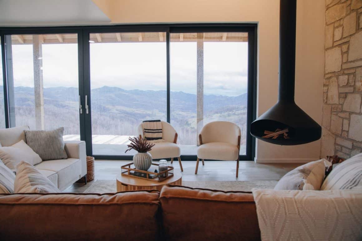livingul de la Hilltop Munteni Apuseni, decorat modern, cu mult alb, semineu metalic, negru, minimalist, si ferestre mari cu privire panoramica spre munte - una din destințaii romantice din țară.