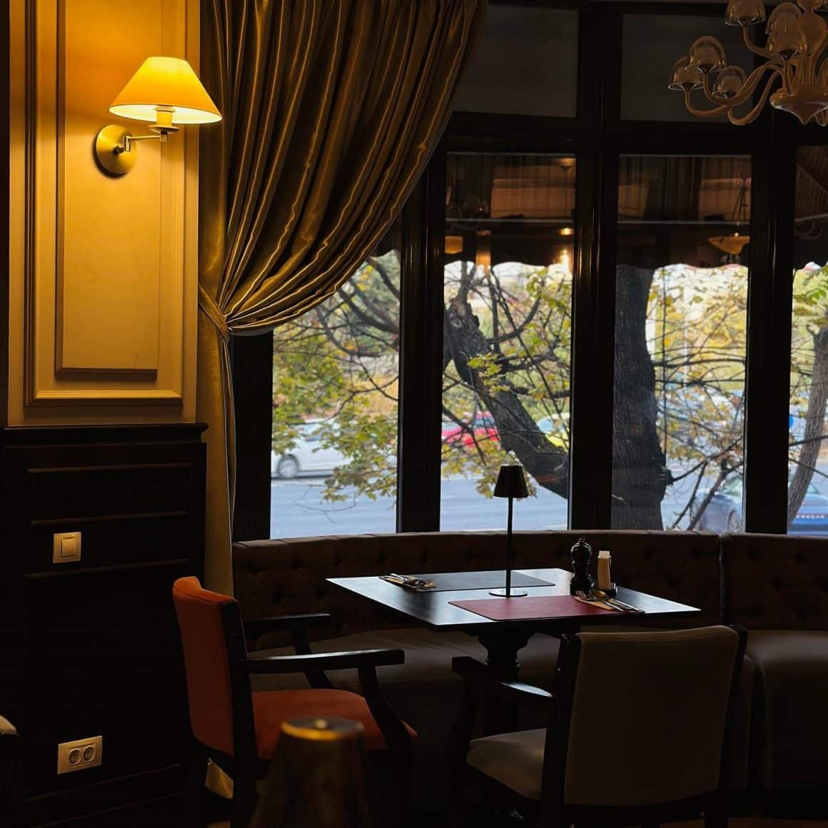 masa in dreptul unei ferestre cu draperii, intr-un decor clasic, cu o veioza aprinsa, la Samuelle, restaurante romantice din București 